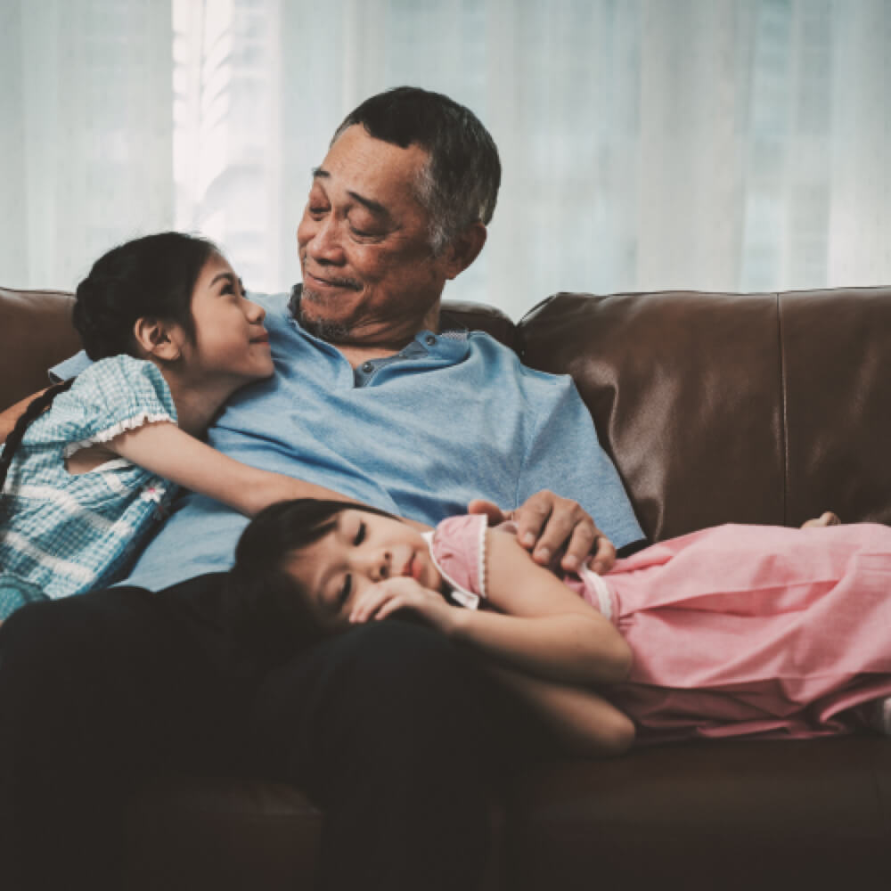 An elderly man and two children are lounging on a couch.