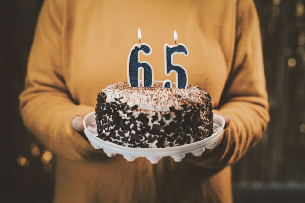 Someone is holding a birthday cake with candles that read "65" on top.