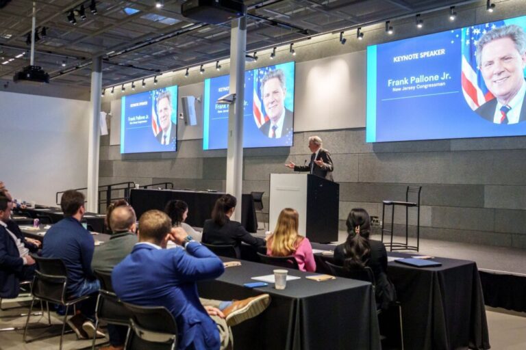 A speaker addresses an audience with screens behind him.