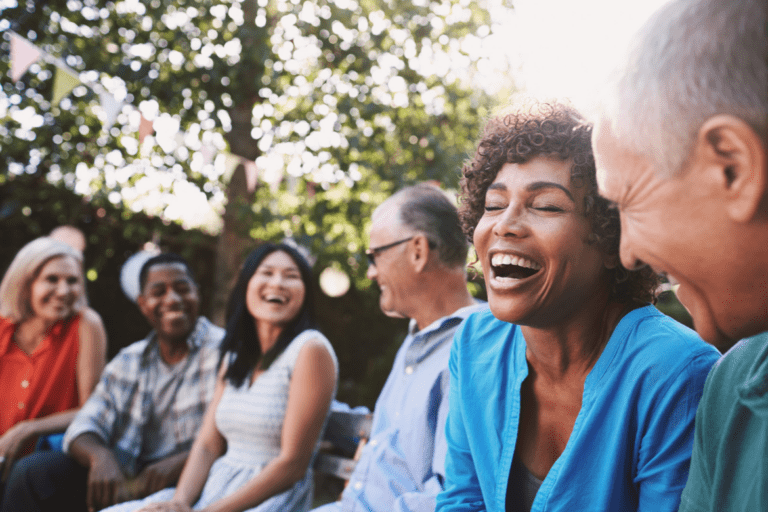 A group of people sitting outside on a sunny day, laughing and enjoying each other's company.