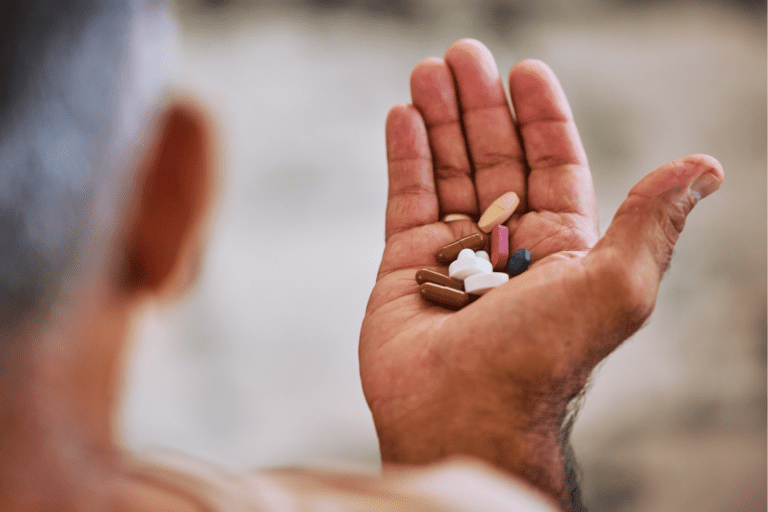 A person holds various pills and capsules in their open hand.