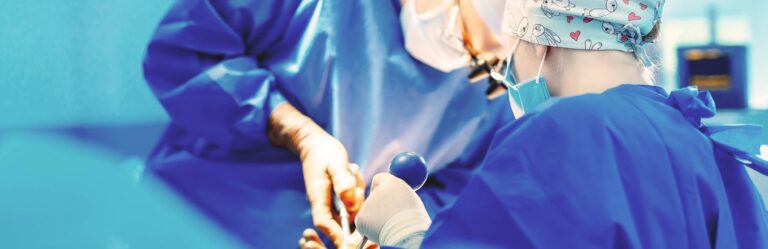 Surgeons wearing blue scrubs and face masks perform a surgical procedure in an operating room.