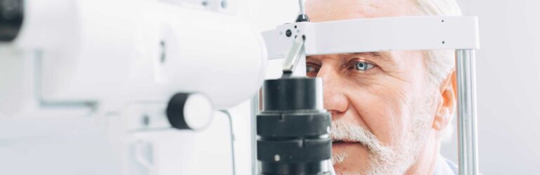 An elderly man undergoing an eye examination using a slit lamp machine at an eye clinic.