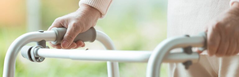 A close-up of an elderly person's hands gripping the handles of a walker.