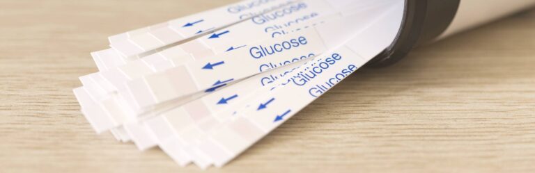 Close-up of a container dispensing glucose test strips arranged on a wooden surface.