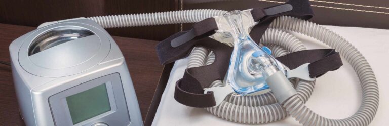 A CPAP machine with a face mask and hose, typically used for sleep apnea treatment, is placed on a bedside table.