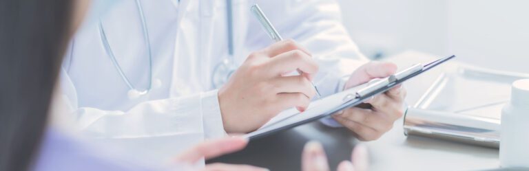 Doctor in a white coat writing on a clipboard during a consultation with a patient.