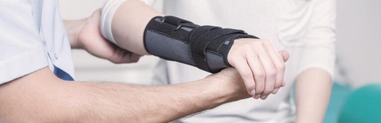 A person wearing a wrist brace is being assisted by another person in a medical setting.