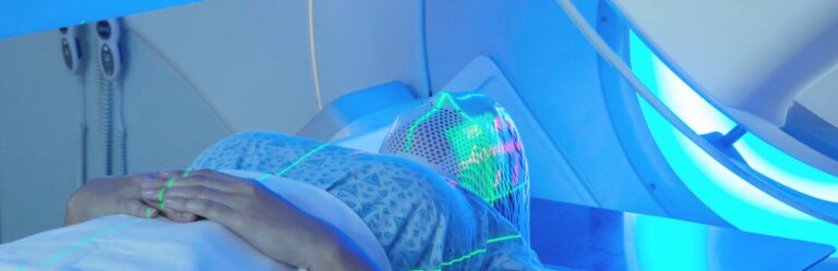 Patient undergoing a medical procedure involving advanced imaging technology while lying on a table, with a mesh head covering and green laser lines visible on their body.