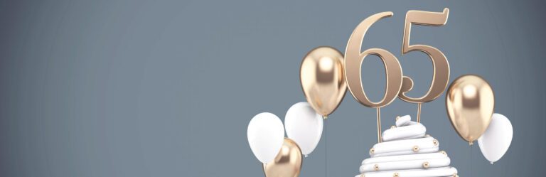 A white cake topped with golden "65" and surrounded by white and gold balloons against a gray background.