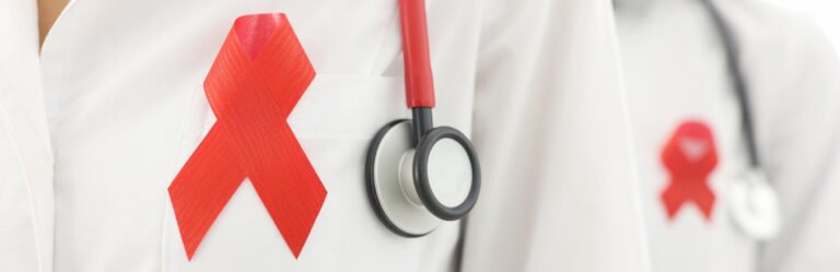 Close-up of two doctors wearing white coats with red HIV/AIDS awareness ribbons and stethoscopes.