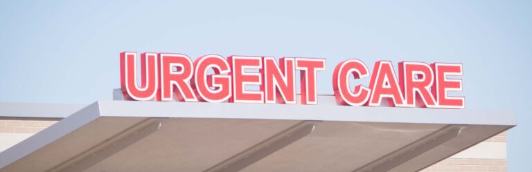 A red "Urgent Care" sign displayed on top of a building against a clear blue sky.