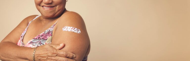 A person with a patterned band-aid on their upper arm smiles while holding their arm.