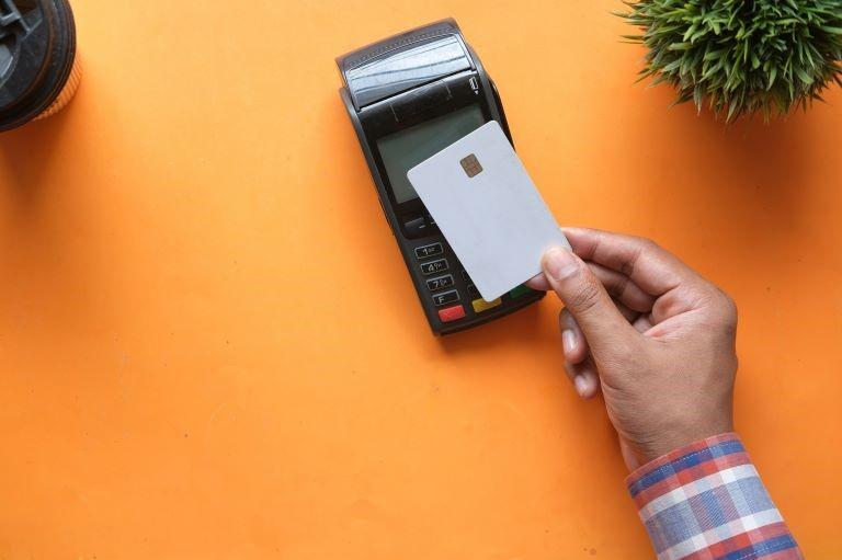 Hand holding a blank payment card above a credit card machine.